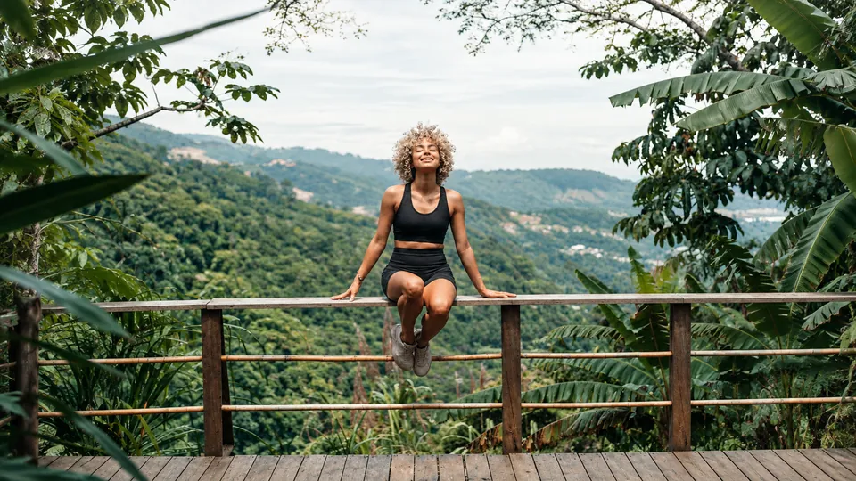 Woman seated on a railing overlooking lush hills